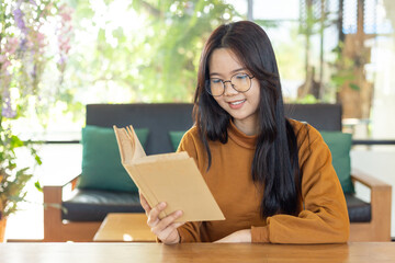 Smiling woman reading a book in a cozy bright cafe with natural greenery, expressing relaxation, learning, focus, and a peaceful modern lifestyle moment.