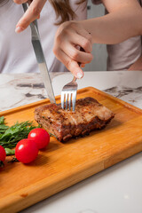 A hand cuts into a tender steak on a wooden board, surrounded by vibrant cherry tomatoes and herbs