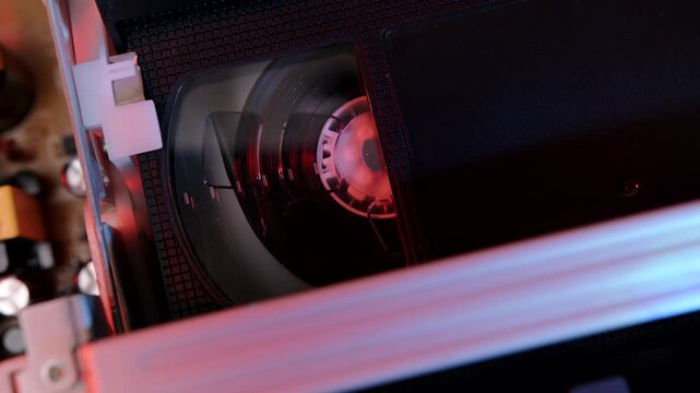 Magnetic tape of VHS video cassette reeling inside VCR during playback of television image and sound close-up