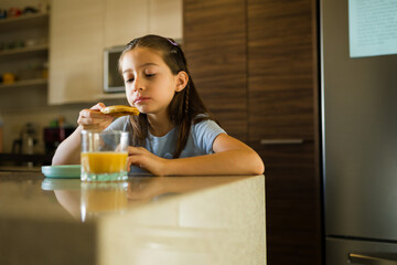 Girl enjoying breakfast at kitchen counter, eating pancake and drinking orange juice at home