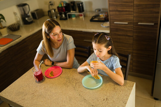 High angle view of a mother and daughter eating breakfast in the kitchen, enjoying a healthy family meal together at home - Powered by Adobe