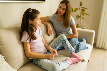 Mother and daughter talking together on a comfortable sofa in their living room, sharing a meaningful family discussion