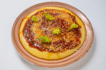 Creamy polenta topped with rich meat ragù and grated cheese, garnished with fresh celery leaves on a clean white background. Minimal and appetizing food presentation