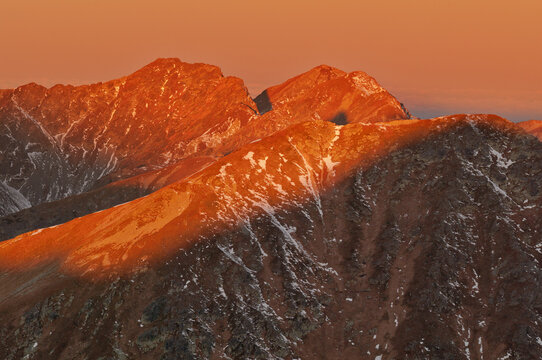 Aerial view of the dramatic peaks of Bystra, tinged with fiery sunset hues against the snow-dusted slopes, Pribylina, Zilina Region, Slovakia.