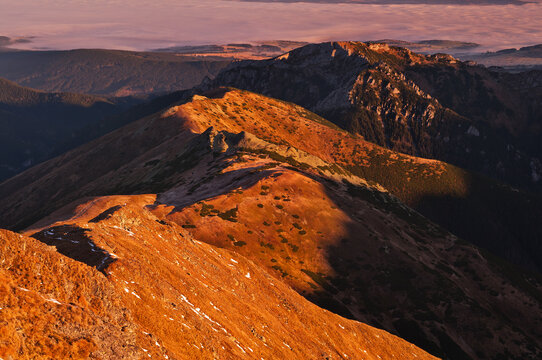 Aerial view of sun-kissed mountain ranges cast long shadows, revealing textured peaks and valleys in a symphony of light and shadow, Pribylina, Zilina Region, Slovakia.