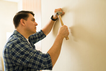 Man driving nail into living room wall with hammer, installing new decor or making household repairs