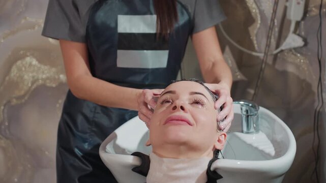 caucasian businesswoman at salon basin enjoying therapeutic temple and scalp massage, stylist fingers kneading temples, client smiles with eyes closed, wellness mood, towel around neck, pampering