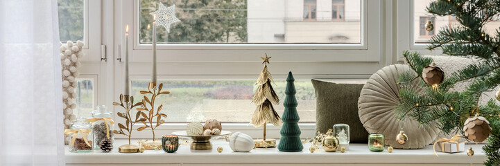 Obraz premium Christmas window sill with candles, trees and ornaments in gold and green. Cozy and natural festive arrangement with soft daylight.