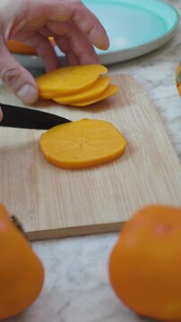 vertical shot. A man cutting persimmons. Slicing persimmons for a salad on a wooden board. Delicious persimmon salad. Healthy eating.