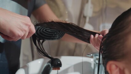 close-up wet hair detangling at salon sink showing hands combing long dark strands for smoothing and shine, professional stylist using gentle technique and conditioner to remove knots, calm atmosphere