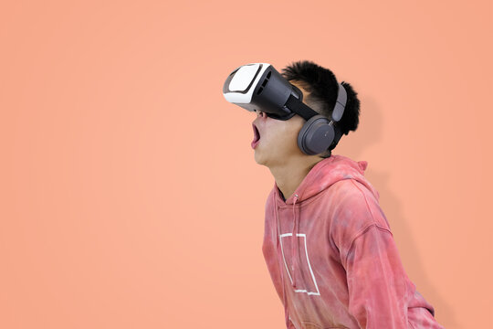 Intense young Asian man in a pink tie-dye hoodie wearing a virtual reality headset and headphones, making a focused or grimacing expression in studio background