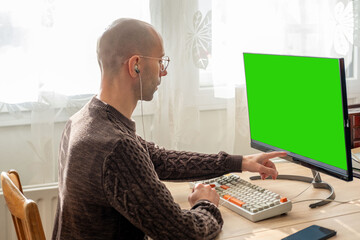 Programmer, young man working at computer with blank green screen, coding process, modern worker solving problems, specialist digital tasks, home office environment promoting productivity and calm