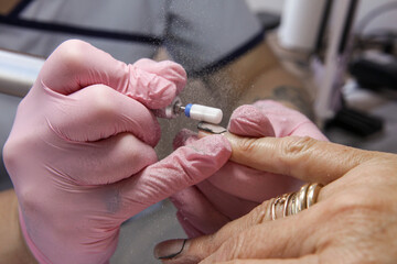 Close-up of a nail technician&rsquo;s gloved hands shaping a client&rsquo;s nails with an electric nail drill in a clean, modern salon.