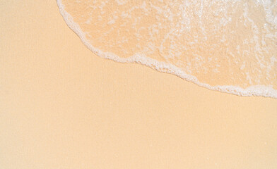 Close-up aerial view of  sea water with white foam from a gentle wave meeting the fine, light beige sand of a tropical beach. The image a serene and tranquil natural scene. 