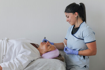 Fototapeta premium Mature woman receiving a professional microneedling facial treatment performed by a &nbsp;cosmetologist at a modern beauty clinic or spa salon.