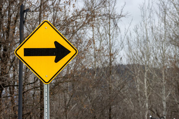 Canada, Quebec, 27 November 2025 : Bright yellow road sign points right among bare winter trees.