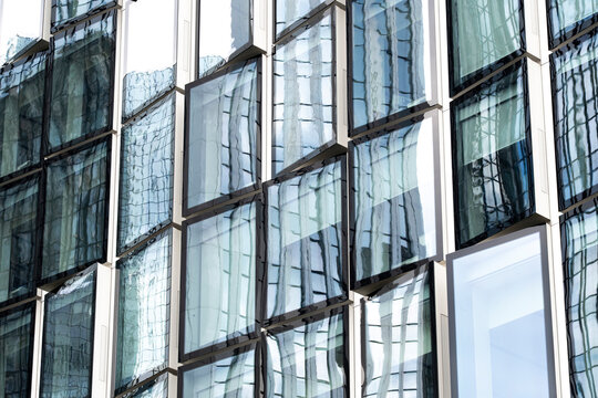 Architecture and reflection interacting across the glass facade where pattern, symmetry and abstract elements from modern office windows form precise geometric lines and urban design