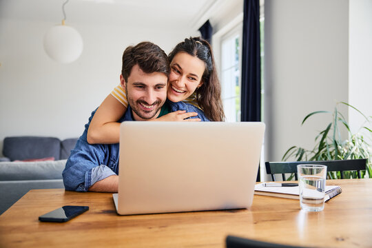 Young couple hugging while shopping online using laptop at home - Powered by Adobe