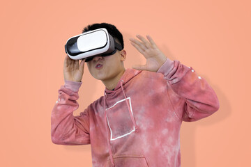 Excited young Asian man wear hoodie reacting with joy while wearing a virtual reality headset, symbolizing the thrilling first experience in studio background