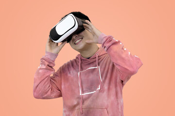 Excited young Asian man wear hoodie reacting with joy while wearing a virtual reality headset, symbolizing the thrilling first experience in studio background