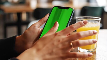 Woman Using Smartphone with Green Screen Display at Cafe Next to Orange Juice Modern Lifestyle and Technology Integration. - Powered by Adobe