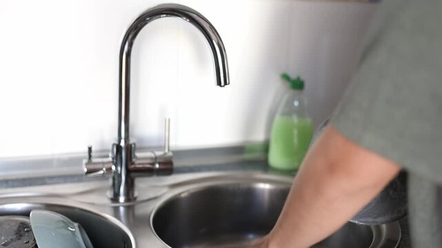 Washing dishes with soapy water in the kitchen sink to maintain hygiene and cleanliness.
