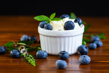 A bowl of cottage cheese decorated with blueberries and leaves on a wooden table