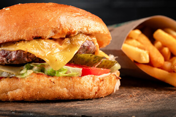 Juicy cheeseburger with melted cheddar, fresh lettuce, tomato, and beef patty served with golden french fries on a rustic wooden table. Classic fast food meal, hamburger combo, american diner style.