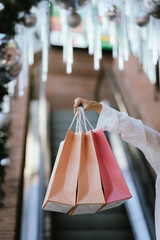 A smiling woman carries multiple shopping bags while walking outdoors near festive Christmas decorations, creating a cheerful holiday shopping vibe.