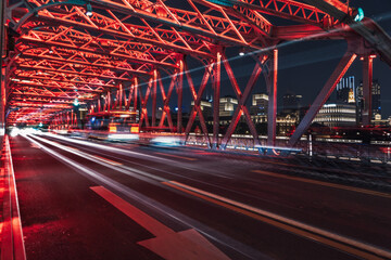 View of red metal bridge adorned with lights as vehicles speed across, creating streaks of light against the dark cityscape, Shanghai, Shanghai, China.