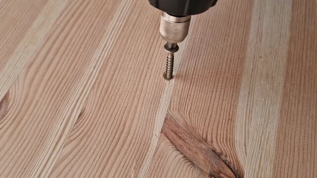 Close-up of a power drill unscrewing a metal screw from a light wooden surface with visible grain, construction, handyman services, or DIY home projects - Powered by Adobe