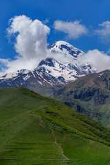 Fototapeta premium Mount Kazbek towering above green hillside hiking trail