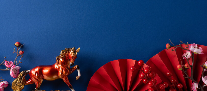 A festive scene with a golden horse statue, red fan and blossoms set against a deep blue backdrop, conveying luck, prosperity and traditional celebration. - Powered by Adobe