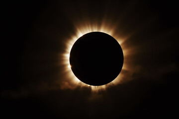 Obraz premium A total solar eclipse darkens the sky, revealing the brilliant, spiky solar corona radiating around the blacked-out sun.