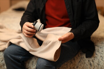 Fototapeta premium Adult caucasian male using fabric shaver on beige blanket in cozy room