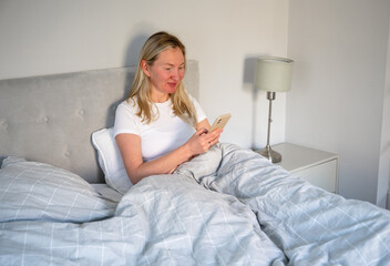 woman using smartphone while relaxing in cozy bedroom