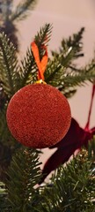 A red, glitter-covered, shatterproof Christmas ornament ball hanging on a Christmas tree.