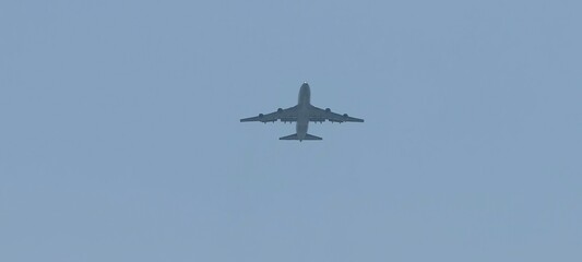 Wide-body Boeing 747 aircraft flying against a clear blue sky. Viewed from below, the image highlights the aircraft’s undercarriage, wings, and engines,ideal for illustrating aviation, aerospace.