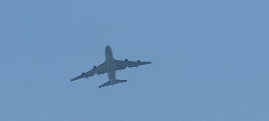Wide-body Boeing 747 aircraft flying against a clear blue sky. Viewed from below, the image highlights the aircraft’s undercarriage, wings, and engines,ideal for illustrating aviation, aerospace.