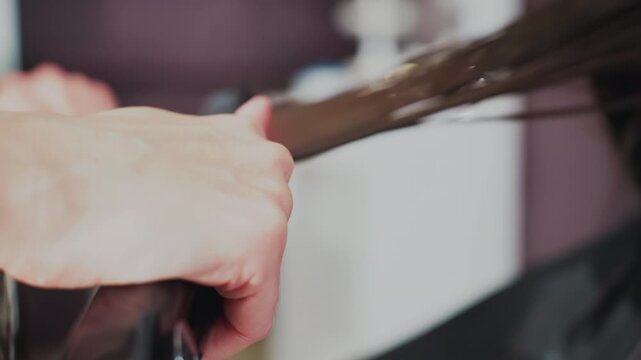 closeup flat iron gliding through hair, white woman client receives thermal straightening as stylist clamps heated plates and smooths sections, red heat indicator and steady hands emphasize precise