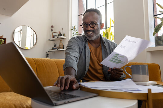 Happy Mature Man Reviewing paperwork with Laptop Nearby