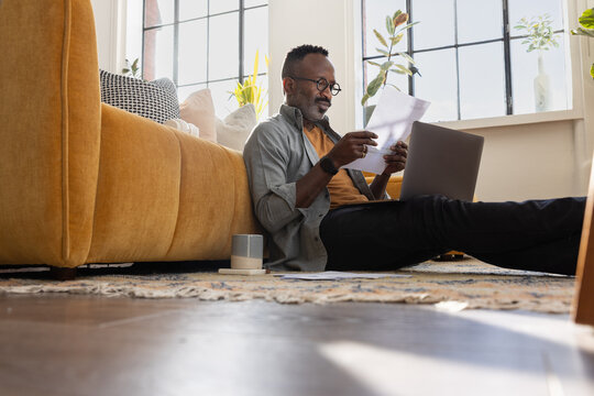 Focused Man looking at paperwork and using a laptop in bright home