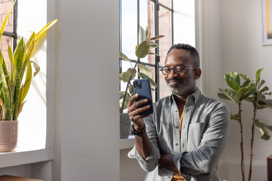 Man happily looking at smartphone by the window with lots of house plants