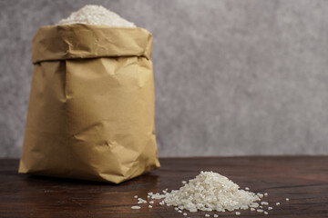 A brown paper bag filled with white rice, placed on a wooden table with a small pile of raw grains in front. Perfect for charity, zakat fitrah, and Ramadan food themes.