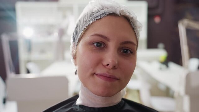 caucasian woman in salon wearing cap, closeup during chemical hair treatment preparation, esthetician prepping scalp, disposable cap and cape, calm confident expression, soft clinical lighting, salon - Powered by Adobe