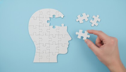 White human head shaped jigsaw puzzle with a missing piece being completed by a hand holding the final part on a clean light blue background