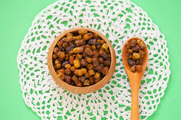 Heaithy bee product bee bread or perga granules from fermented bee pollen in wooden bowl on hand crocheted napkin on green background. Perga is natural source of vitamins and healhy minerals