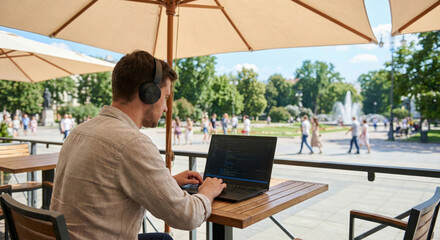 A programmer enjoys nature working on a laptop in the park under a sunshade
