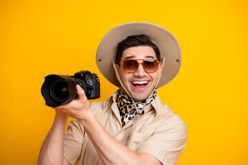 Cheerful photographer with safari hat and camera ready for travel adventure against bright yellow...
