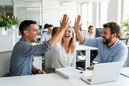 Three office workers joyfully high five in a bright open workspace during the day